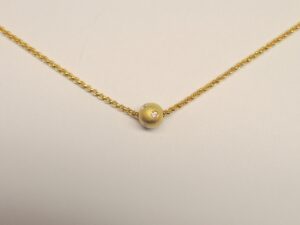 Die Goldkugel aus 750 Gelbgold ist mit 5 Diamanten besetzt und befindet sich an einer vergoldeten Erbskette