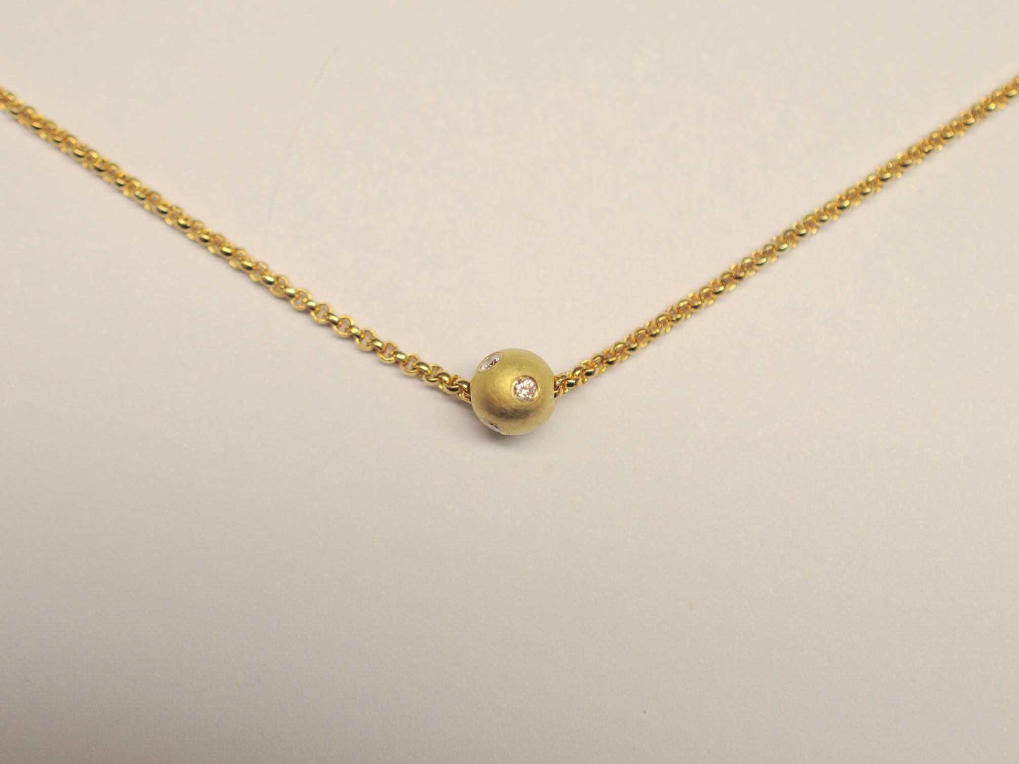 Die Goldkugel aus 750 Gelbgold ist mit 5 Diamanten besetzt und befindet sich an einer vergoldeten Erbskette