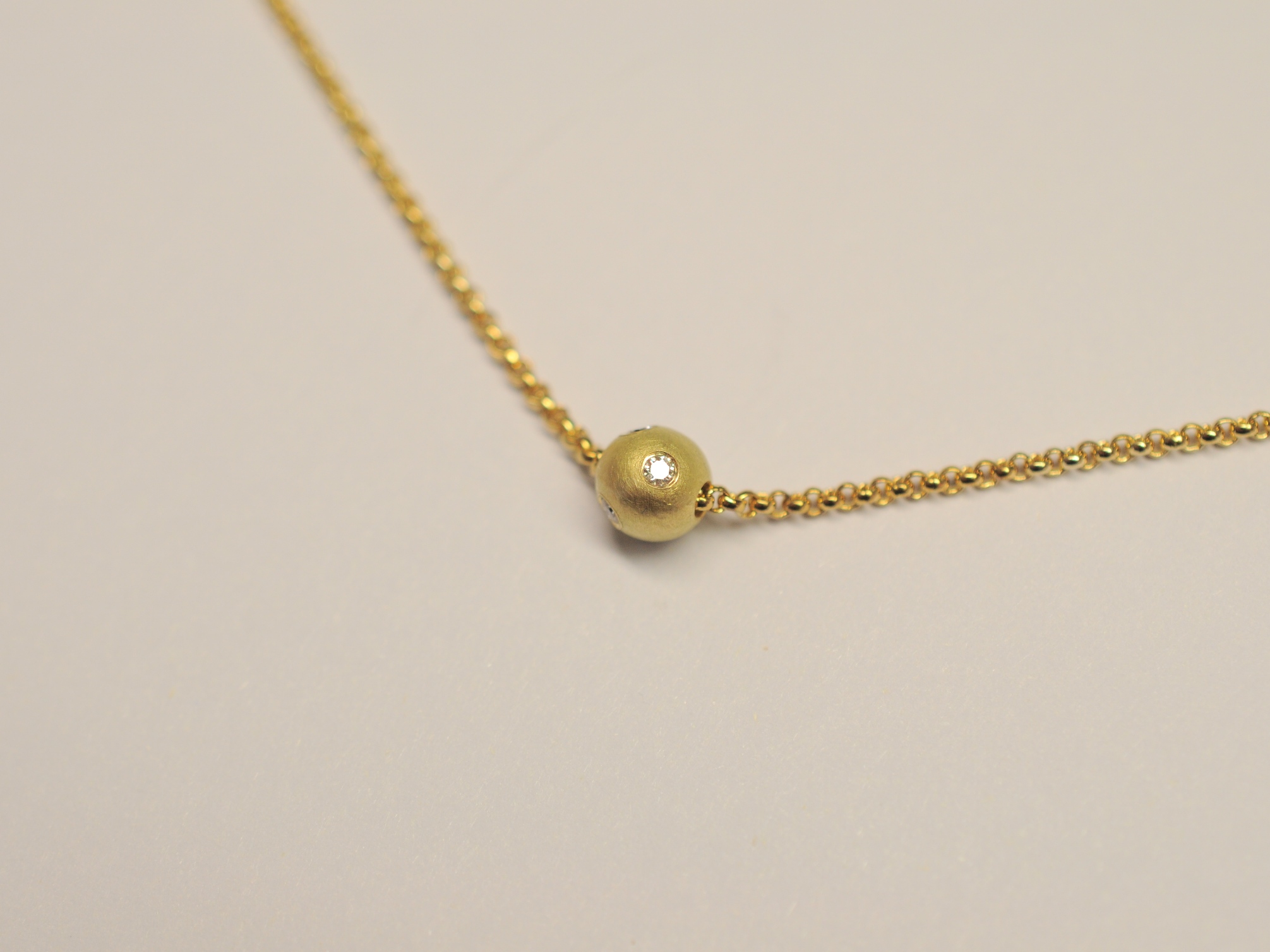 Die Goldkugel aus 750 Gelbgold ist mit 5 Diamanten besetzt und befindet sich an einer vergoldeten Erbskette